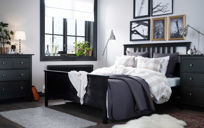 schwarze Einrichtung, Fenster mit schwarzem Rahmen, graue Fußmatte vor dem Bett, zwei Stehlampen mit beweglichem Stand, Blumendeko im Schlafzimmer